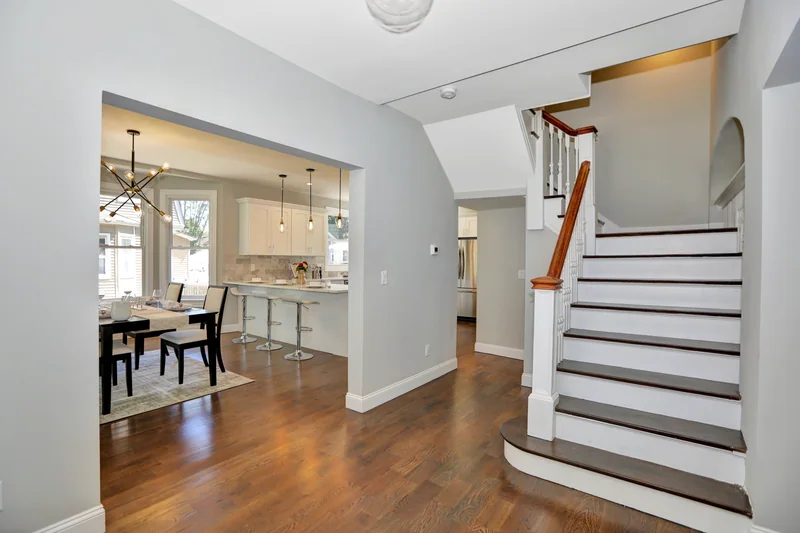 Warm hardwood in an entry hall beside a white staircase, open to a staged dining room
