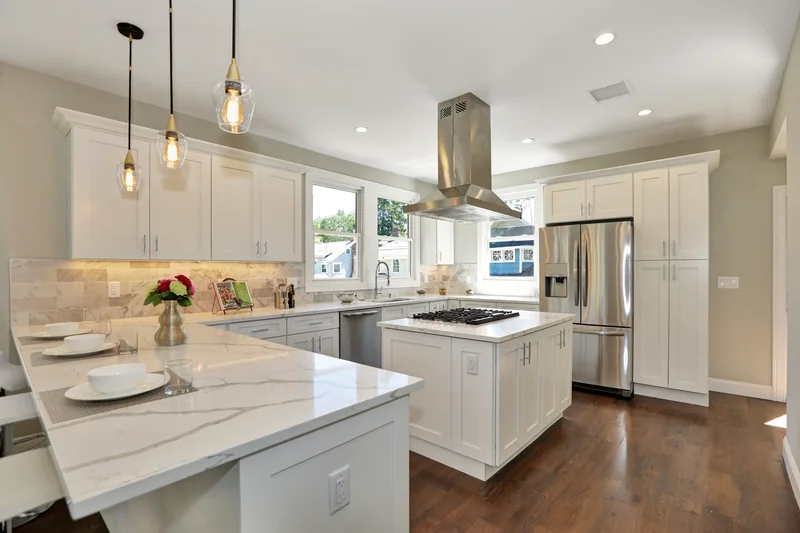 Warm hardwood in a white kitchen with a marble island and a stainless range hood