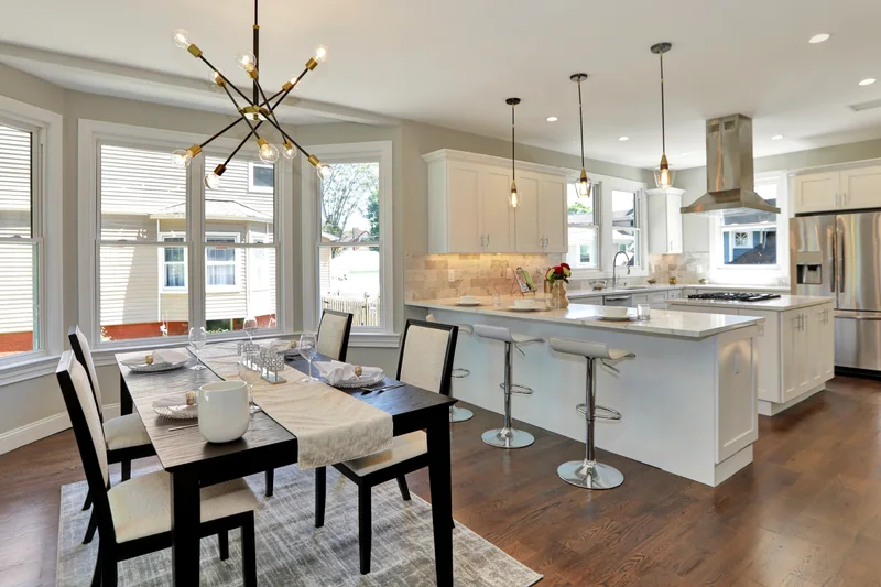 Warm hardwood in a dining area open to a white kitchen with a marble island