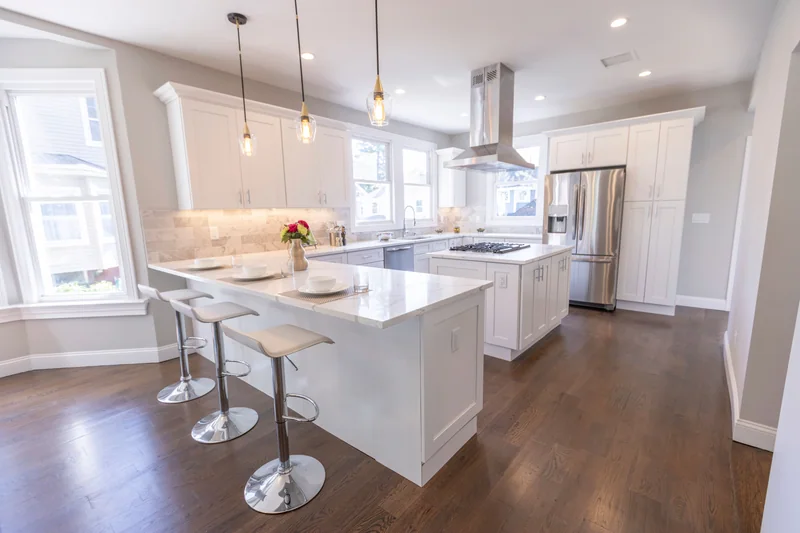 Warm hardwood in a white kitchen with a marble peninsula and three counter stools