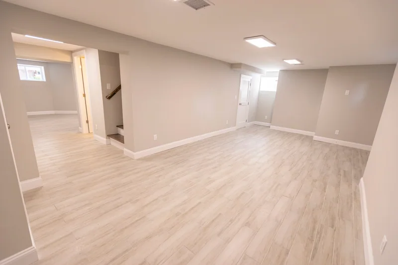 Wide light plank flooring across an open finished lower level past a stair opening