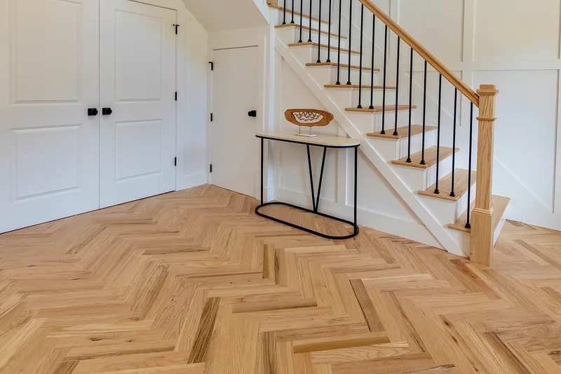 Herringbone hardwood in an entry hall at the foot of a stair with black metal balusters