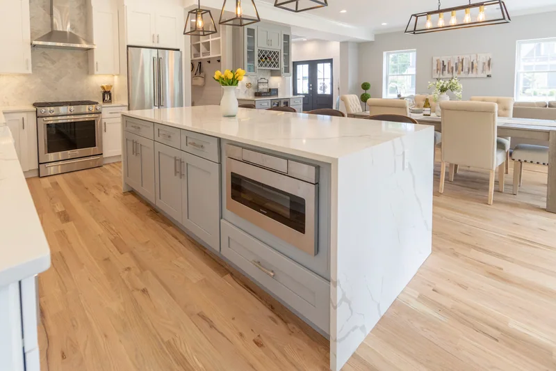 Pale hardwood in a kitchen with a marble-topped island and a built-in microwave drawer