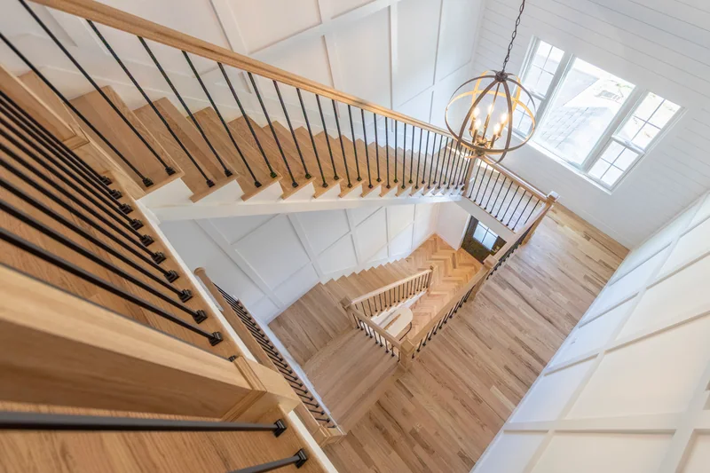 Looking down a stairwell with black metal balusters onto pale plank hardwood