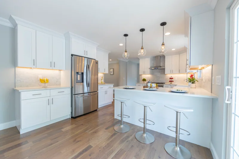 Warm hardwood in a white kitchen with a quartz peninsula and three counter stools