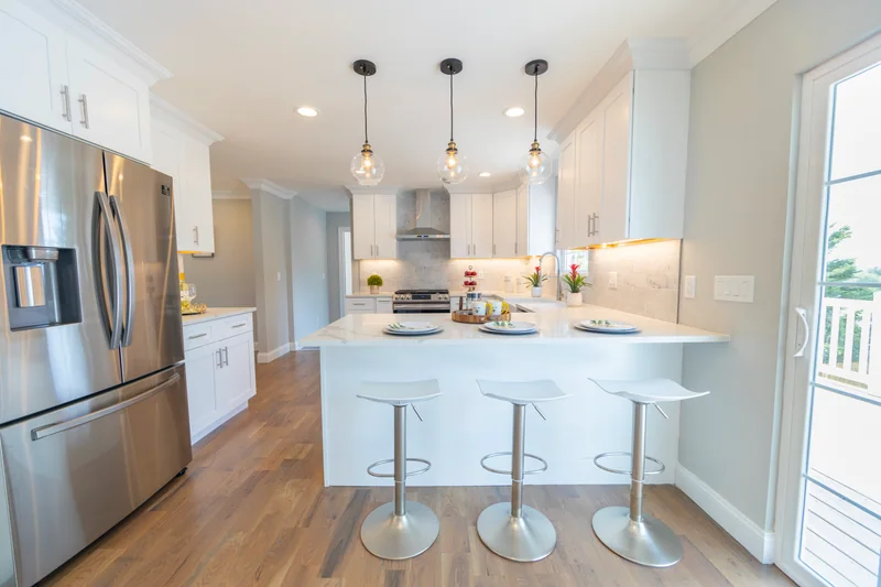Warm hardwood in a white kitchen with pendant lights over a quartz peninsula