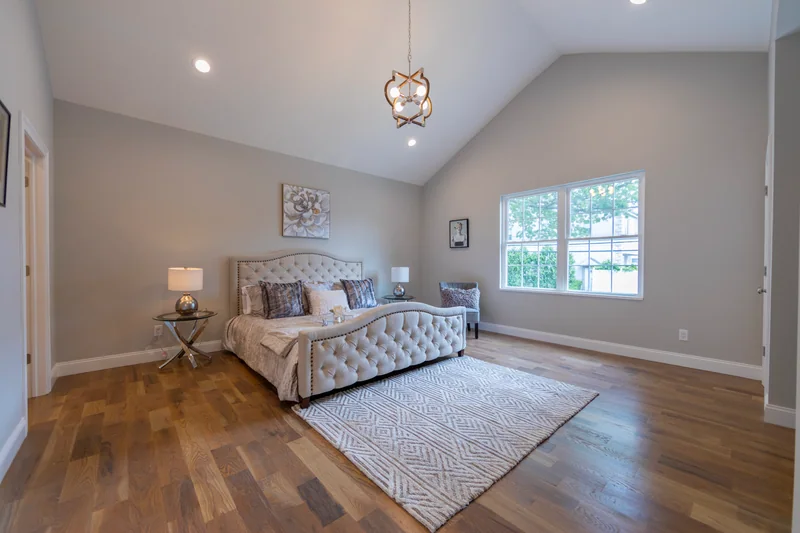 Warm hardwood in a staged bedroom with a tufted headboard under a vaulted ceiling