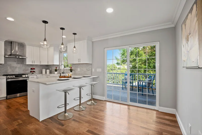 Warm hardwood in a white kitchen with a quartz peninsula, three stools and sliding doors to a deck
