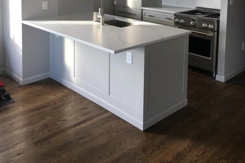 Dark hardwood in a small kitchen with a white peninsula, grey cabinets and two globe pendants