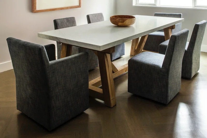 Dark herringbone hardwood in a dining room with a marble-top trestle table and a framed tree-ring print