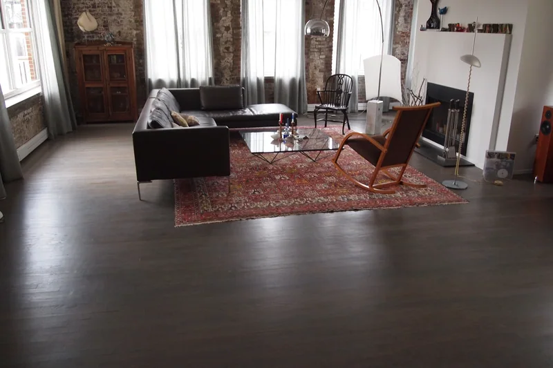 Dark wide-plank flooring in a brick-walled loft living room with tall windows