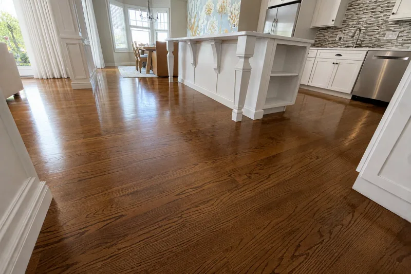 Satin-finish red oak hardwood flooring reflecting daylight across an open living and kitchen space