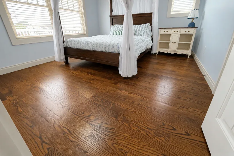 Guest bedroom with refinished red oak hardwood flooring, a dark wood canopy bed and pale blue walls