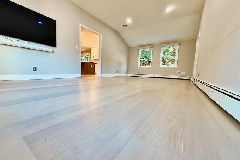 Pale wide-plank hardwood in an empty sloped-ceiling room with a wall-mounted television