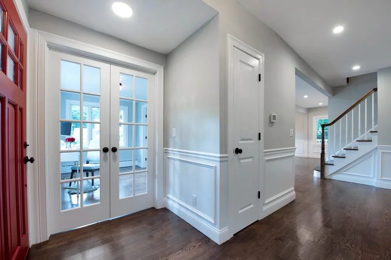Dark-stained hardwood in an entry hall with a red front door and white wainscoting