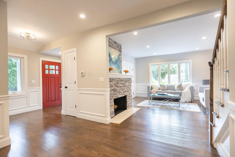 Dark hardwood in a front hall with a red front door and a stacked-stone fireplace beyond