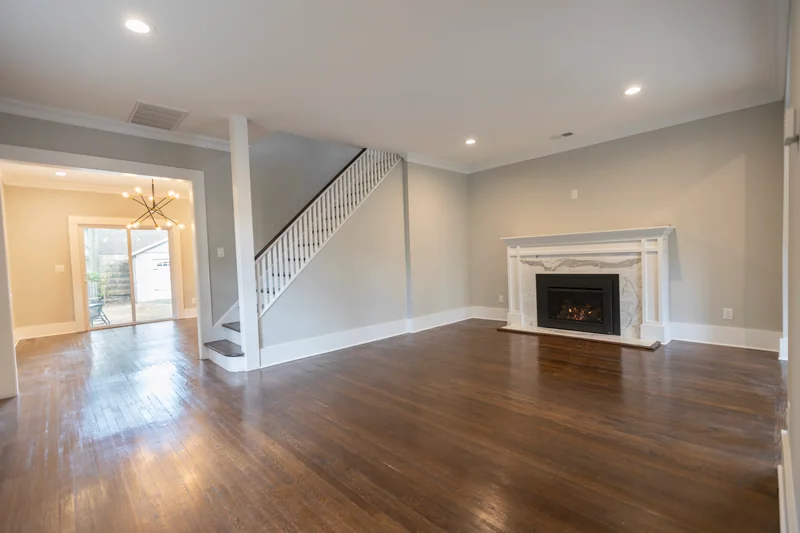 Dark hardwood in an empty living room with a marble fireplace and a white staircase