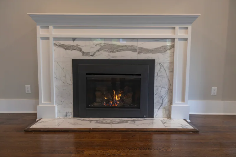 Dark hardwood at the hearth of a gas fireplace with a marble surround