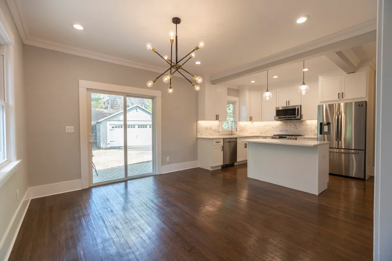 Dark hardwood in an empty dining area with a sputnik chandelier and a white kitchen beyond