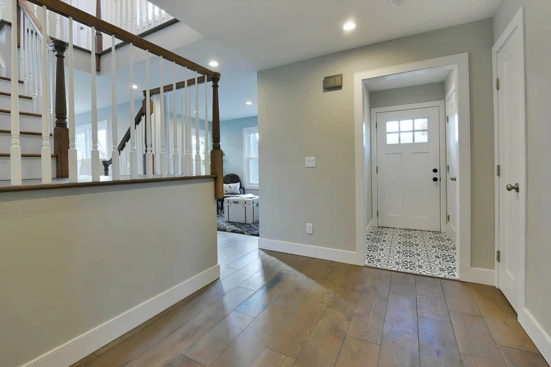 Wide grey-toned hardwood in an entry hall beside a dark-railed staircase