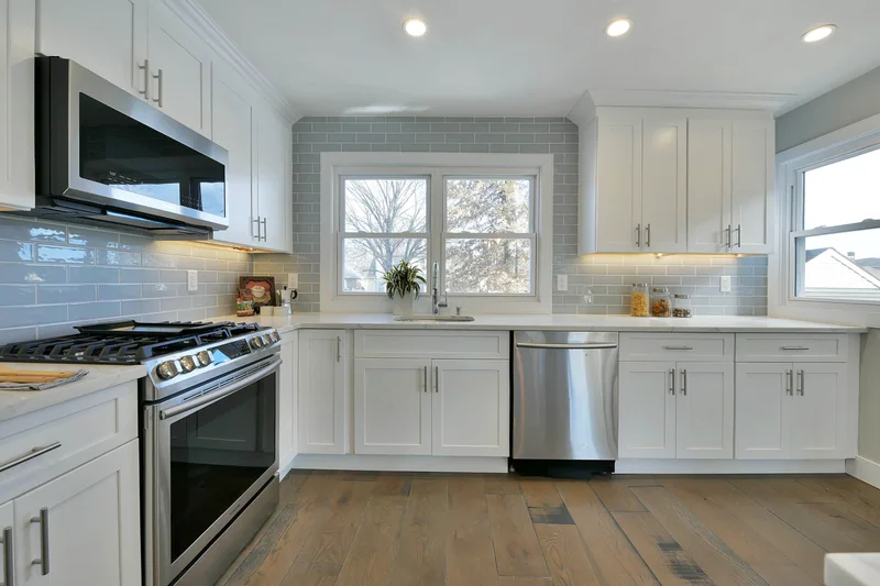 Wide grey-toned hardwood in a white kitchen with a tile backsplash and a stainless range