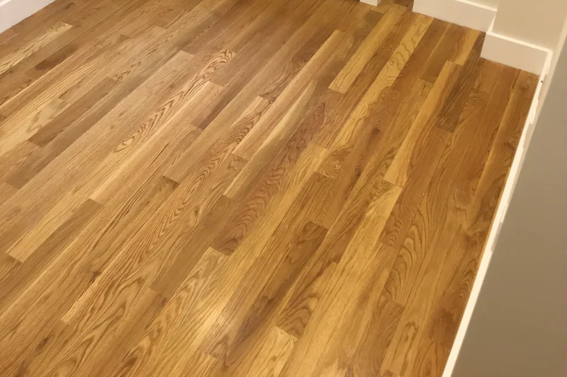 Honey-toned strip hardwood in an empty room corner beneath a white radiator cover