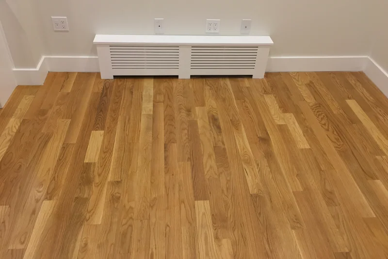 Honey-toned strip hardwood running toward a long white radiator cover in an empty room