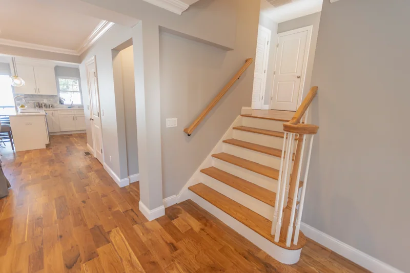 Golden hardwood in a hall beside a stair with white risers, white balusters and a natural-wood handrail