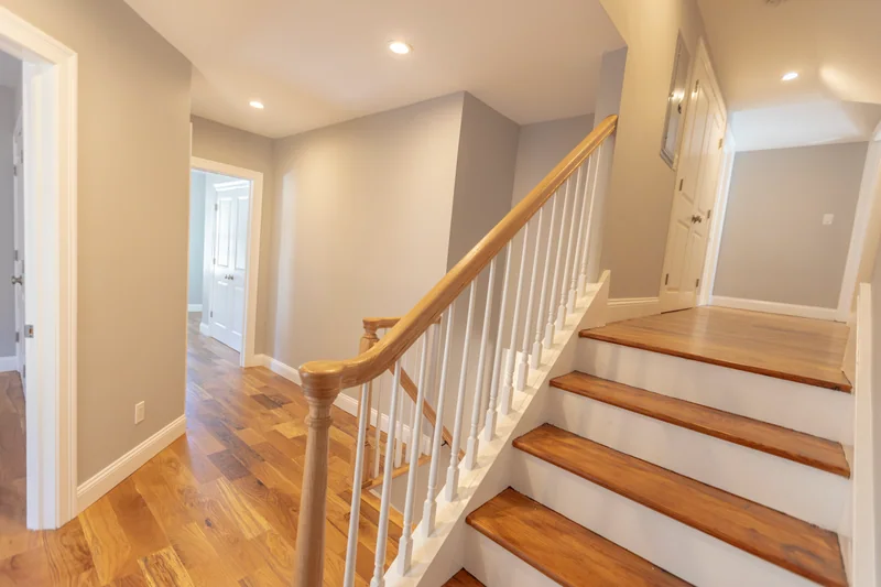 Golden hardwood in a hall at the foot of a stair with white balusters and a natural-wood handrail