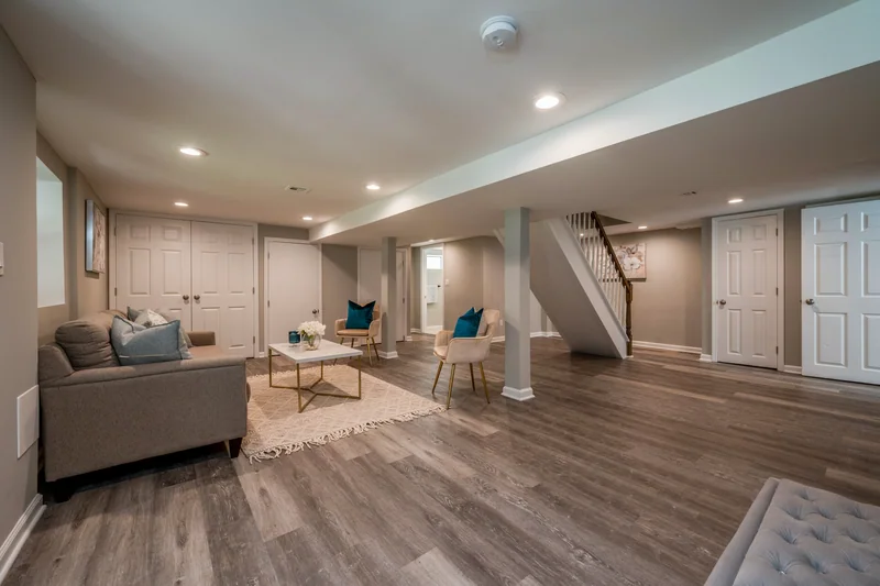 Wide grey-brown plank flooring in a finished lower level with a seating area and stair beyond
