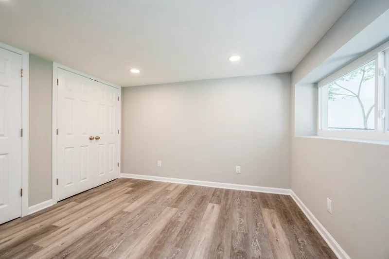 Wide grey-brown plank flooring in an empty lower-level room with a window