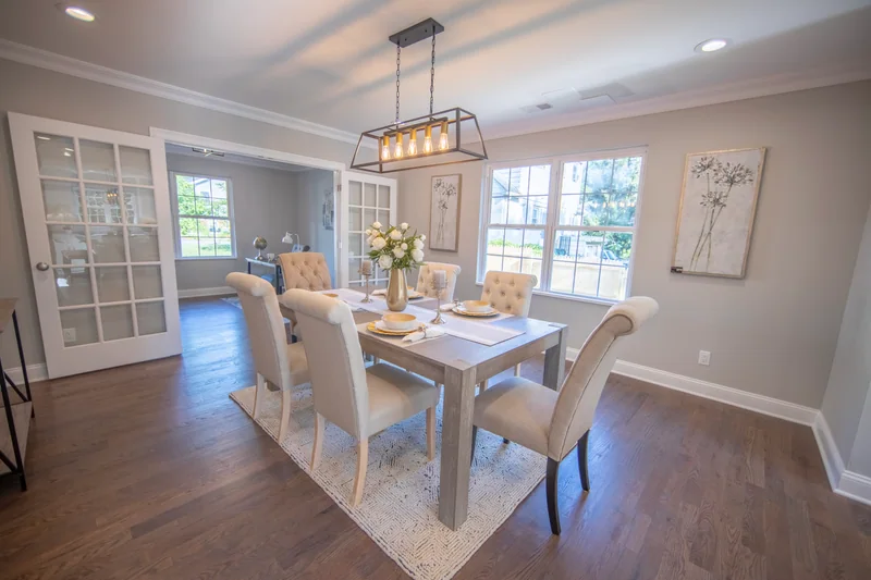 Medium-brown hardwood in a dining room set for six beneath a black linear chandelier