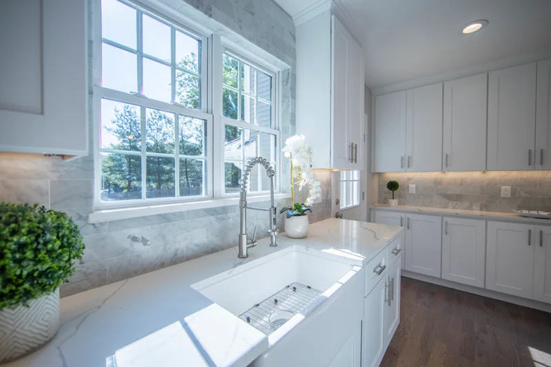 Medium-brown hardwood in a white kitchen with a farmhouse sink and marble backsplash