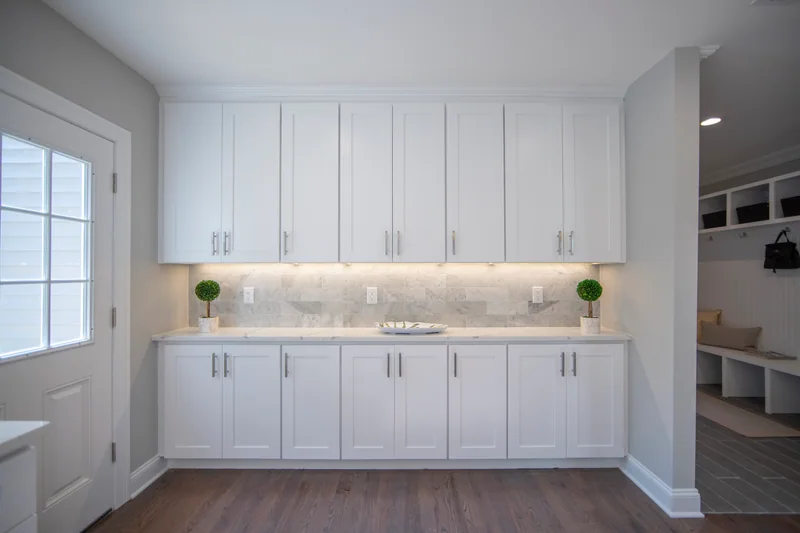 Medium-brown hardwood in a butler’s pantry with white cabinetry and a mudroom beyond