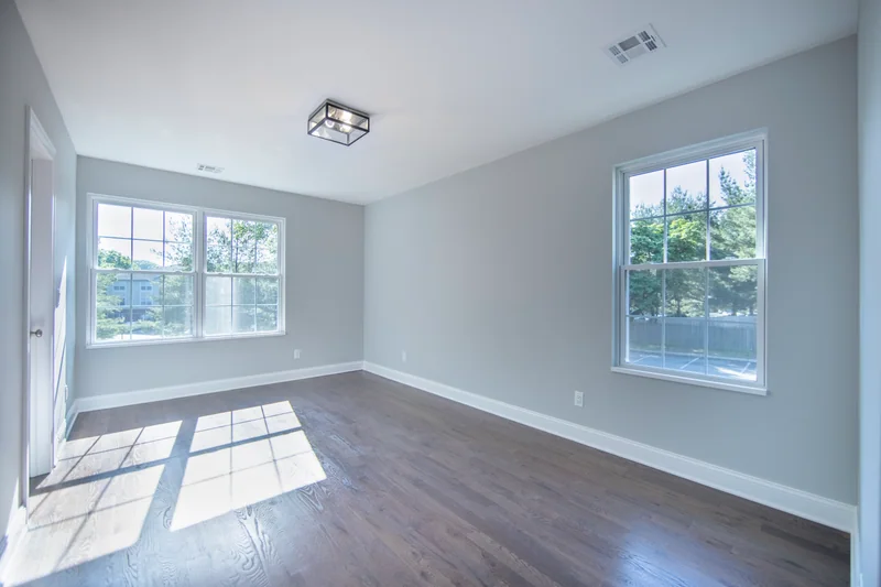 Sunlight across medium-brown hardwood in an empty corner room with two windows