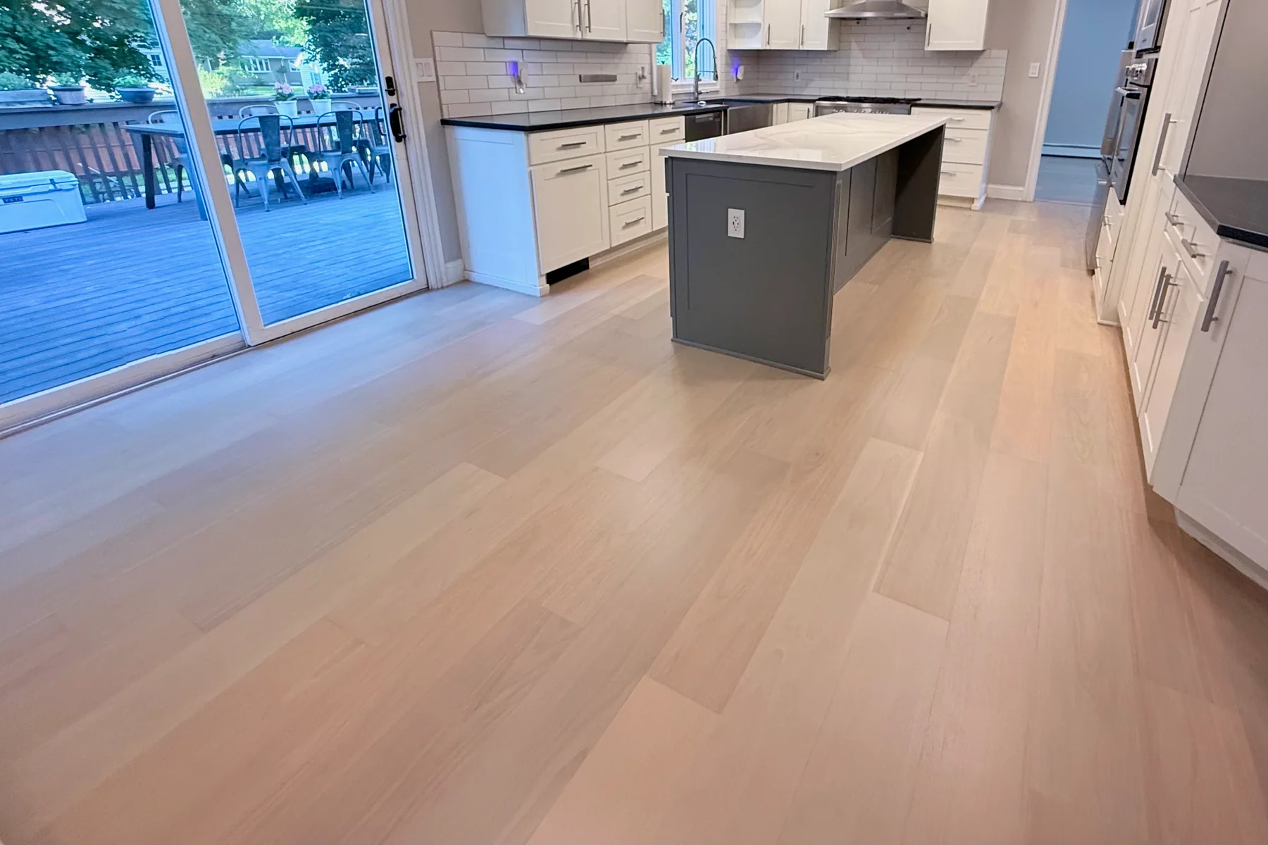 Pale wide-plank hardwood in a kitchen with two grey islands and sliding doors to a deck