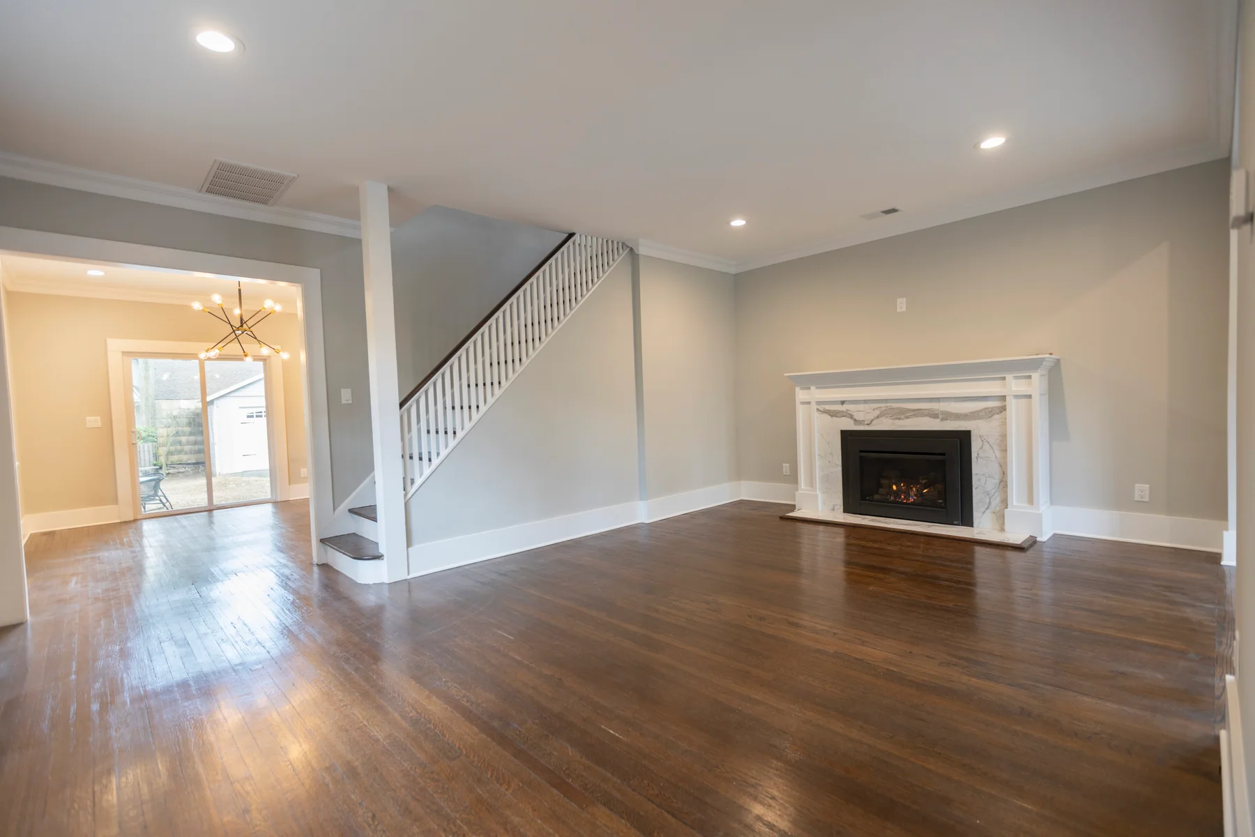 Dark hardwood in an empty living room with a marble fireplace and a white staircase