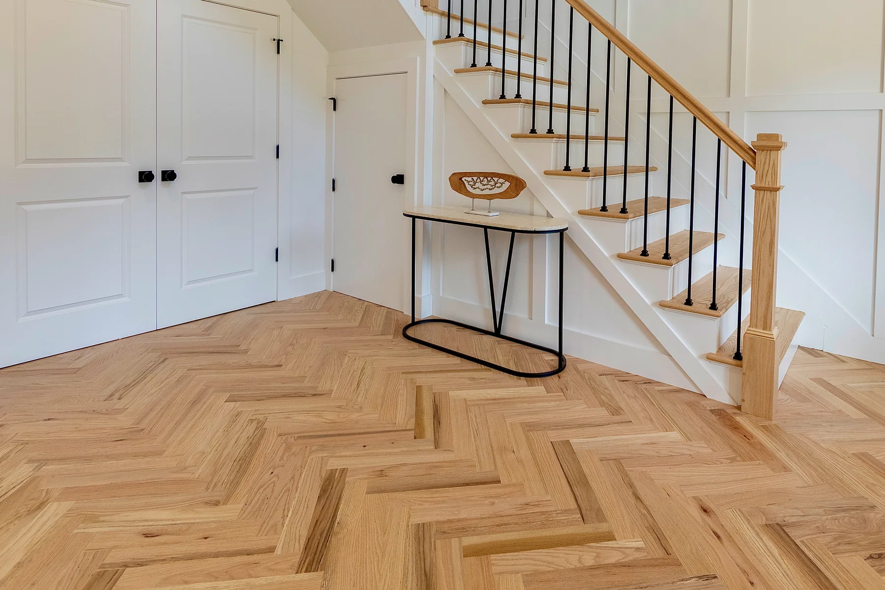 Natural-tone herringbone entry hall with white panelled doors and a white staircase with black metal balusters